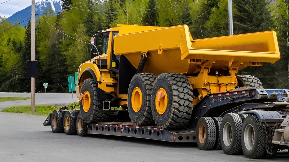Large yellow dump truck on the back of a flatbed truck
