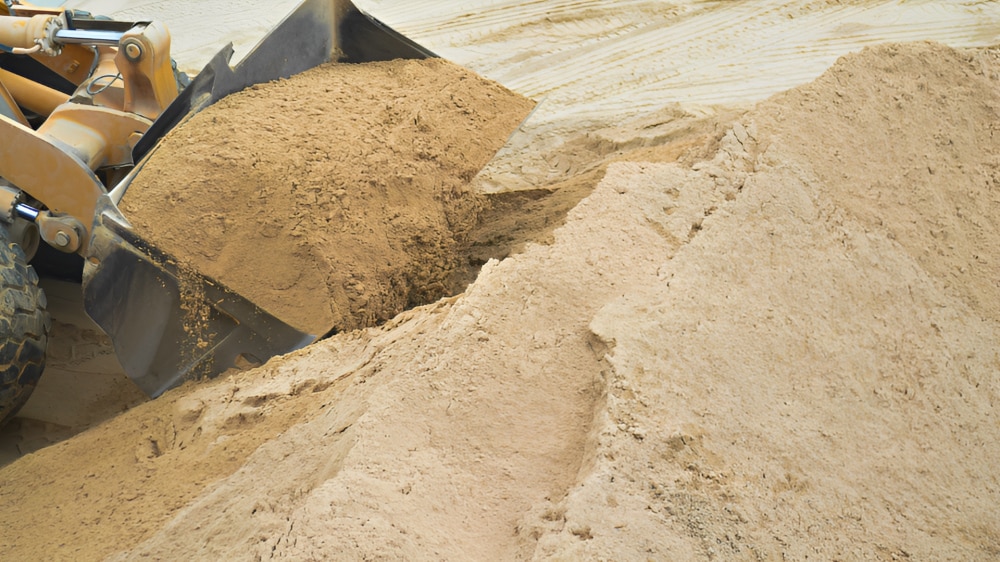 Excavator dumping sand into a large sand pile