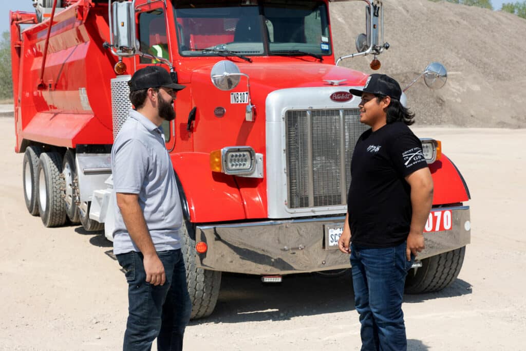 Two aggregate truck drivers meeting in front of red dump truck